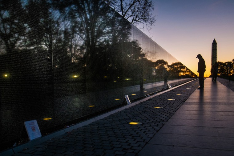 A visitor at the Vietnam War Memorial in Washington passes early in the morning on Veterans Day, Monday, Nov. 11, 2013, to look at the names inscribed on the wall.