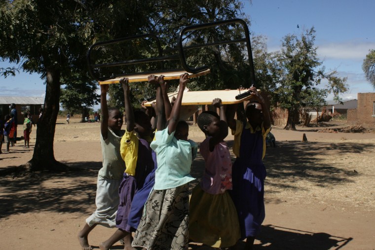 Kids in Malawi carrying K.I.N.D. desks into their classrooms.