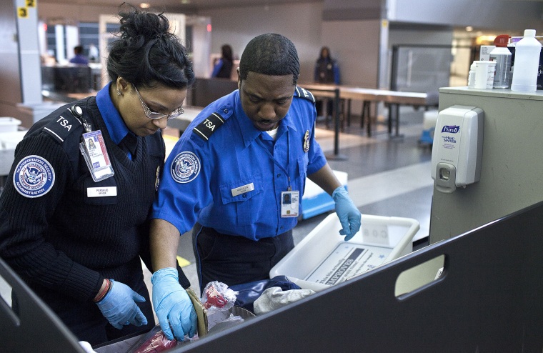Two TSA security agents check a traveler's luggage at John F. Kennedy Airport in New York