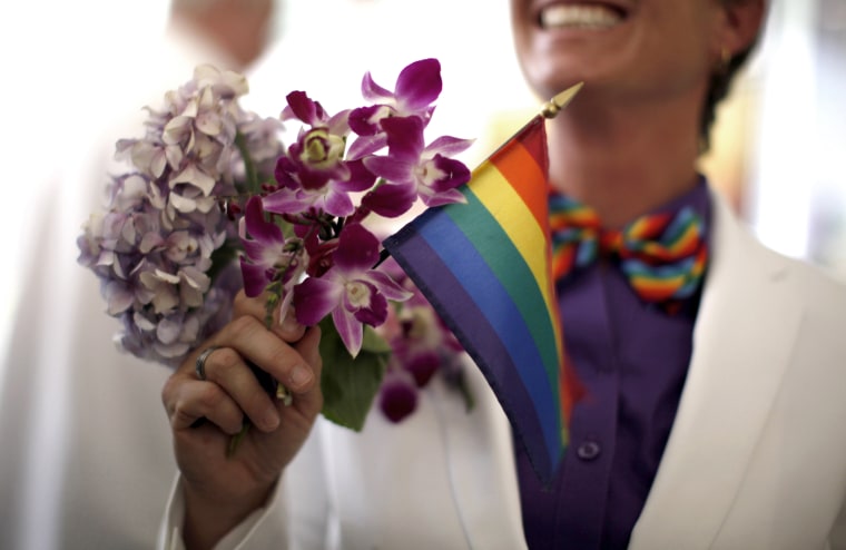 A woman holds a rainbow flag with her bouquet before getting married to her fiancee in West Hollywood, California, July 1, 2013.