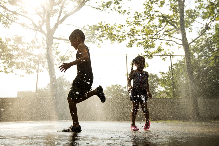 Children run through a sprinkler system installed inside a playground to cool off during a hot summer day in New York