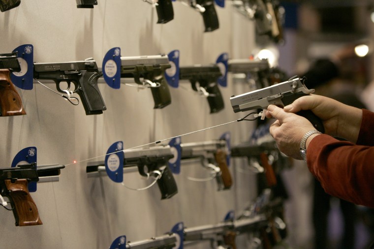 A woman points a handgun with a laser sight on a wall display of other guns during the National Rifle Association convention Friday, April 13, 2007, in St. Louis.