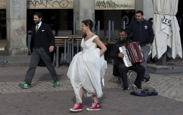 A bride and groom walk past a street musician in Plaza Mayor, Madrid, Spain, Monday, Jan. 20, 2014.