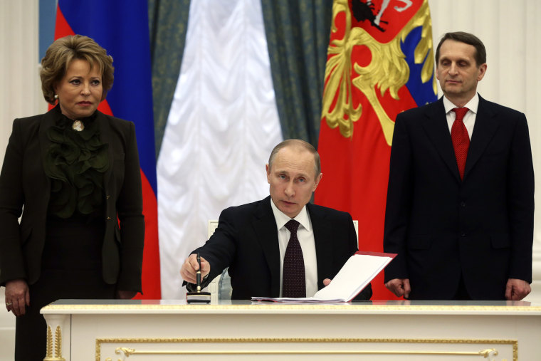 Russian President Vladimir Putin (C) prepares to sign documents as Sergei Naryshkin (R), speaker of the State Duma, Russia's lower parliament house, and Valentina Matviyenko, head of the Federation Council, look on during a ceremony in Moscow's Kremlin Ma