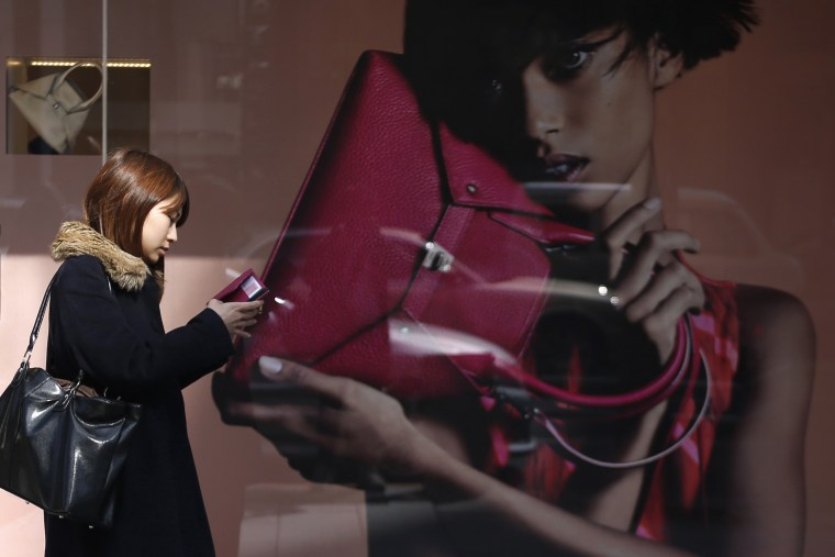 A woman looks at her mobile phone while walking past the display window of a luxury store at Ginza shopping district in Tokyo on Feb. 28, 2014.