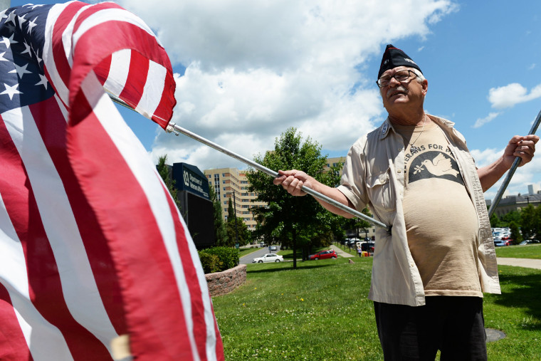 Dan Wilcox, of Albany holds flags in front of the Stratton VA Medical Center in Albany on Thursday, June 19, 2014, for a Veterans for Peace protest to demand adequate healthcare for veterans across the country.