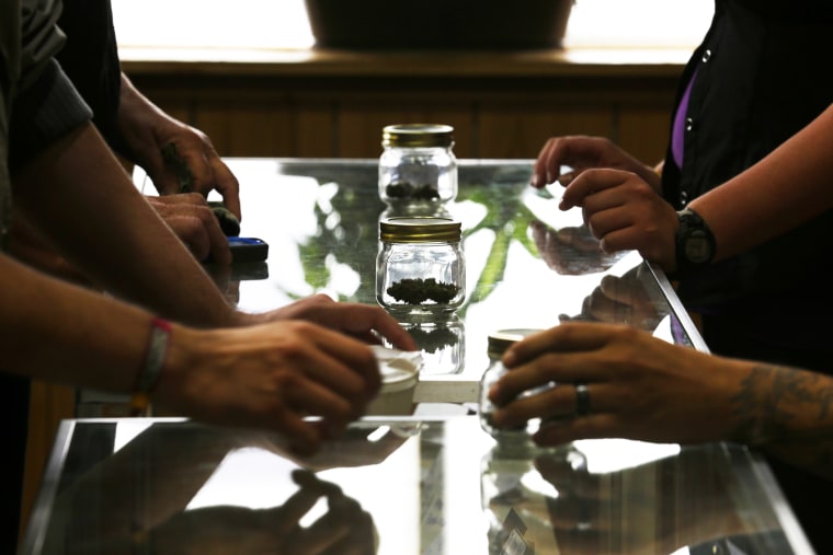 Customers and sales clerks pass jars back and forth as they discuss different strains of recreational marijuana, July 8, 2014, in Bellingham, Wash.