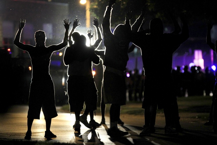 People raise their hands in the middle of the street as police wearing riot gear move toward their position trying to get them to disperse on Aug. 11, 2014, in Ferguson, Mo.