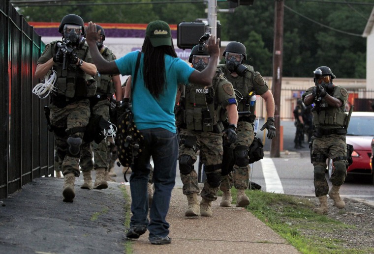 Police wearing riot gear walk toward a man with his hands raised Monday, Aug. 11, 2014, in Ferguson, Mo.
