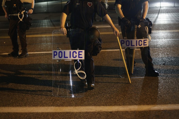 Police officers in riot gear stand in position as demonstrators protest the shooting death of Michael Brown, in Ferguson, Missouri