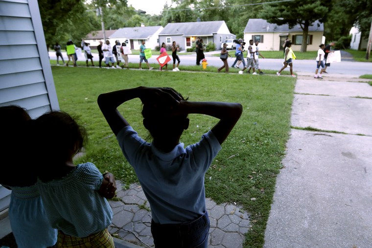Children watch from their home as people march to protest the shooting of Michael Brown in Ferguson, Mo. on Aug. 20, 2014.