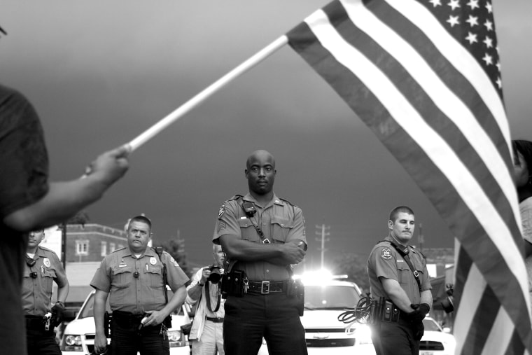 As protestors take over a stretch of road in front of the Ferguson Police Department headquarters, an officer stares down a man waving an American flag on Sept. 10, 2014. The man said he was a Vietnam veteran who is sickened by the death of Michael Brown and no arrest for his killer, officer Darren Wilson.