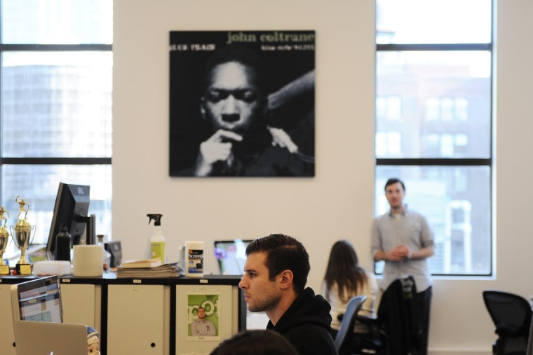 A Spotify employee hard at work while an enlarged album cover of John Coletrane's \"Blue Train\" looks on.
