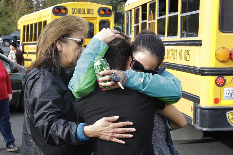 People embrace in front of school busses at a church, Oct. 24, 2014, where students were taken to be reunited with parents following a shooting at Marysville Pilchuck High School in Marysville, Wash. (Photo by Ted S. Warren/AP)