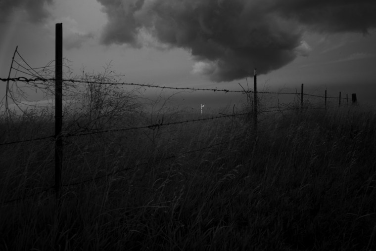 United States flag is illuminated as a storm breaks over a pasture adjacent to the Lakota Community Homes housing project in Rapid City, South Dakota.