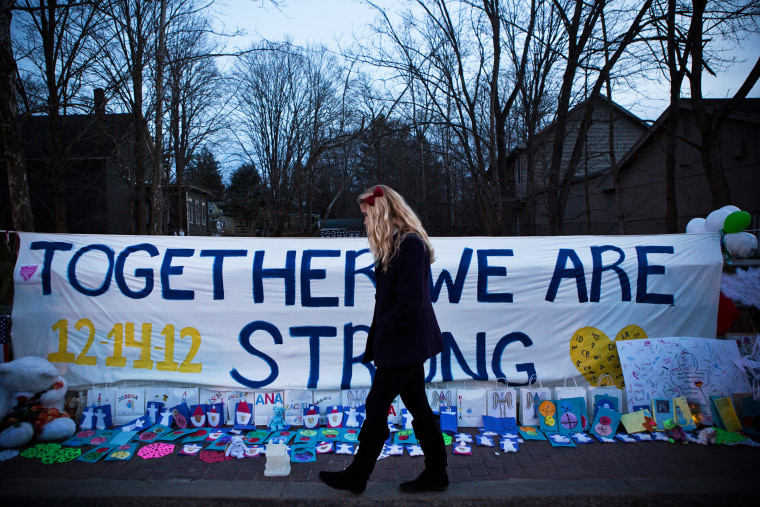 A woman walks past a sign that reads \"Together we are Strong\" at a memorial for those killed in the school shooting at Sandy Hook Elementary School on Dec. 24, 2012 in Newtown, Conn. (Photo by Andrew Burton/Getty)