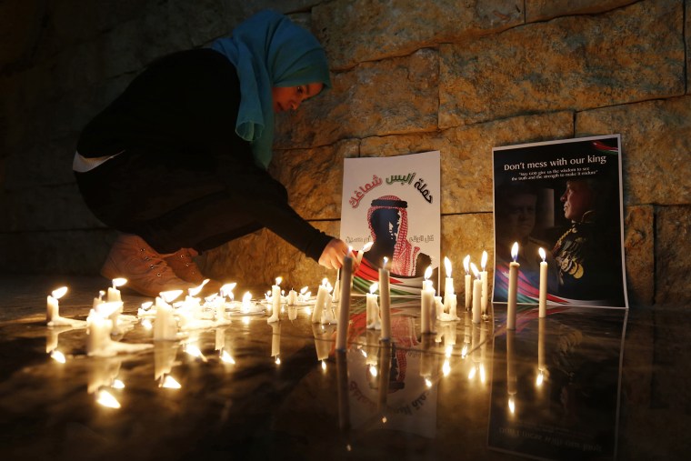 A Jordanian woman lights a candle near a poster of Jordan's King Abdullah (R) and a poster depicting Jordanian pilot Muath al-Kasasbeh during a candlelight vigil in Amman on Feb., 7, 2015. (Photo by Muhammad Hamed/Reuters)