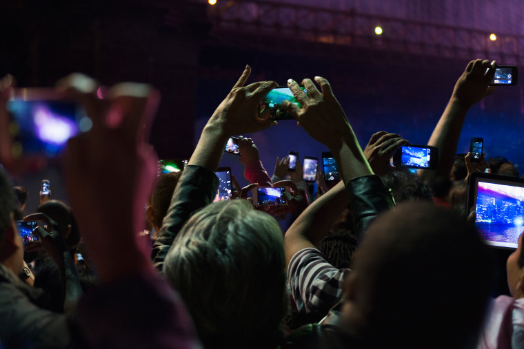 People in crowd take photos on their cell phones at night. (Photo by GS/Gallery Stock)