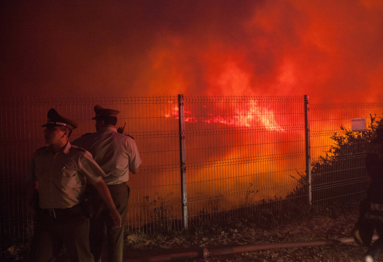 Police officers standby while a forest fire burns the hills of Valparaiso city, northwest of Santiago, Chile, March 13, 2015. As a precaution, 4,500 people were evacuated from Valparaiso and neighboring Vina del Mar. (Photo by Lucas Galvez/Reuters)