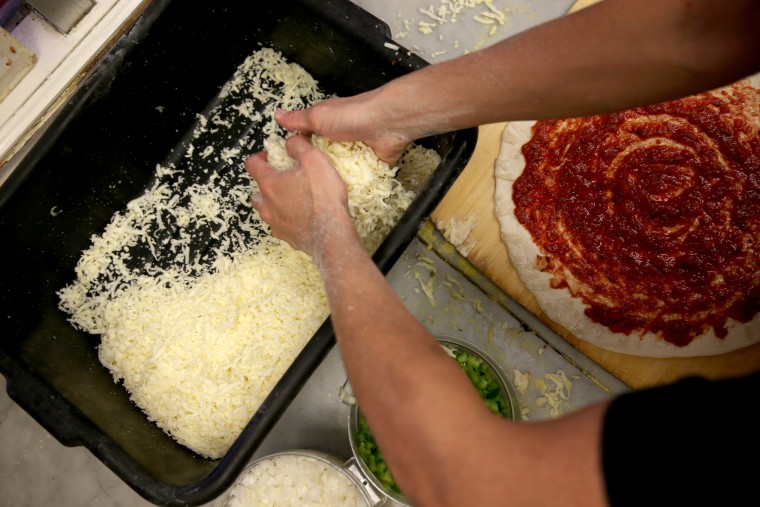 An employee spreads cheese on a pizza. (Photo by Joe Raedle/Getty)