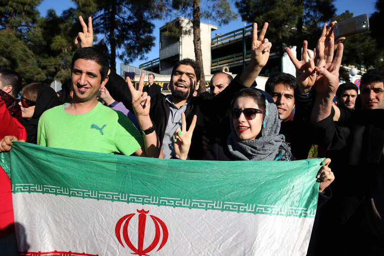 Iranians flash the victory sign as they hold their country's flag while waiting for arrival of Foreign Minister Mohammad Javad Zarif from Lausanne, Switzerland, at the Mehrabad airport in Tehran, Iran, April 3, 2015. (Photo by Ebrahim Noroozi/AP)