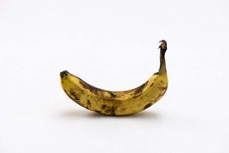 A yellow and black over ripe banana displayed on a white table.