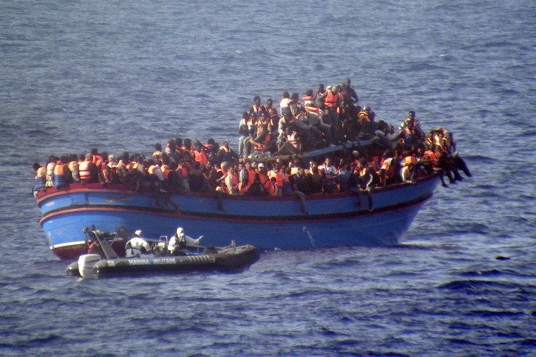 A motor boat from the Italian frigate Grecale approaches a boat overcrowded with migrants in the Mediterranean Sea on June 29, 2014.