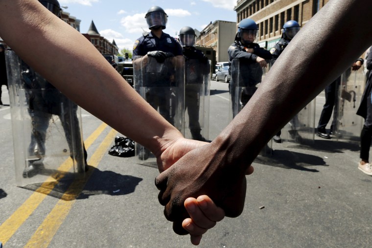 Members of the community hold hands in front of police officers in riot gear outside a recently looted and burned CVS store in Baltimore, Md, on April 28, 2015. (Photo by Jim Bourg/Reuters)