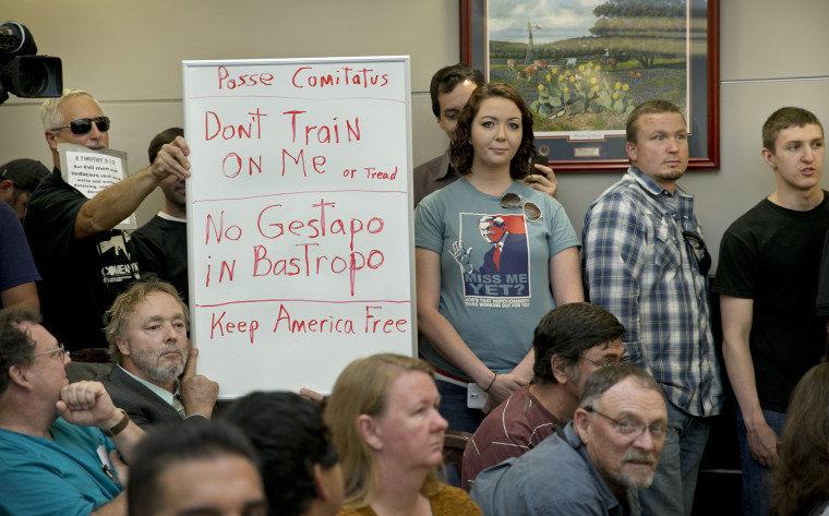 Bob Welch, standing at left, and Jim Dillon, hold a sign at a public hearing about the Jade Helm 15 military training exercise in Bastrop, Texas, Monday April 27, 2015.
