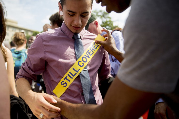 Demonstrator Ron Busby, with Center for American Progress, right, places a \"Still Covered\" sticker onto Kory Masen after the U.S. Supreme Court ruled 6-3 to save Obamacare tax subsidies, June 25, 2015. (Photo by Andrew Harrer/Bloomberg/Getty)