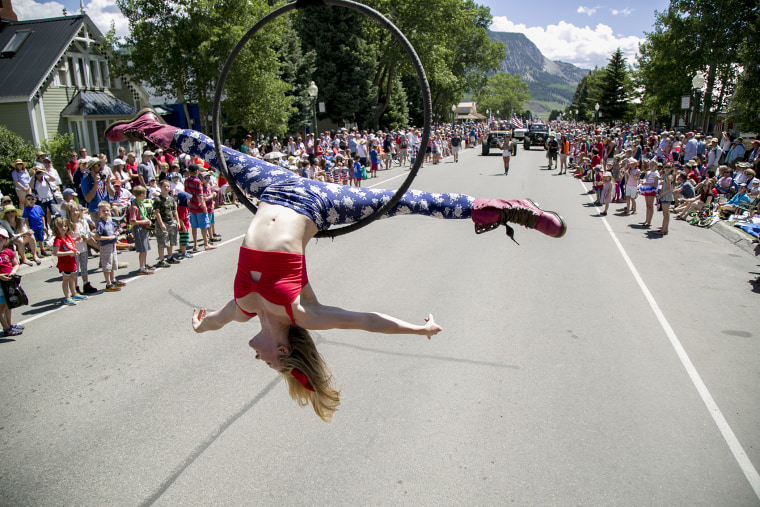 An aerial performer does the splits while hanging from a moving tow truck while performing at the Crested Butte 4th of July parade.