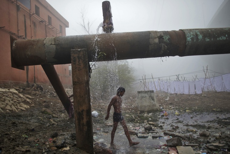 A man bathes under a broken water pipeline at a riverside on a cold winter morning in New Delhi, India on Jan. 20, 2014 (Photo by Ahmad Masood/Reuters).