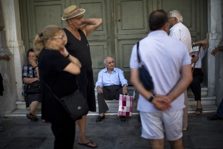 Pensioners sit at the main gate of the national bank of Greece as they wait to withdraw a maximum of 120 euros ($134) for the week in central Athens, July 13, 2015. (Photo by Emilio Morenatti/AP)