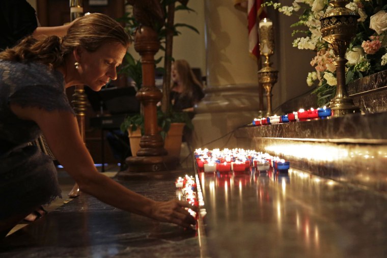 A woman places a candle on the altar during a prayer service for the victims of The Grand 16 theater shooting at the Cathedral of St. John the Evangelist, in Lafayette, La., July 26, 2015. (Photo by Gerald Herbert/AP)