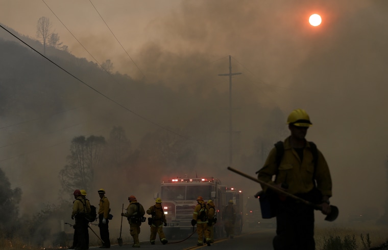 Firefighters walk under smoke from fires along Morgan Valley Road near Lower Lake, Calif., July 31, 2015. A series of wildfires were intensified by dry vegetation, triple-digit temperatures and gusting winds. (Photo by Jeff Chiu/AP)