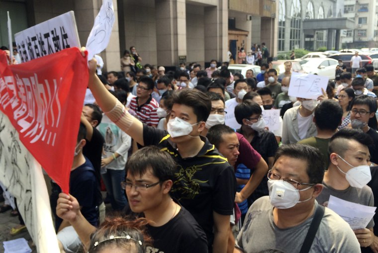 Residents, some wearing masks, hold banners and placards as they stage a protest outside a hotel where officials held daily media conferences in northeastern&nbsp;China's Tianjin municipality, Aug. 17, 2015.&nbsp;