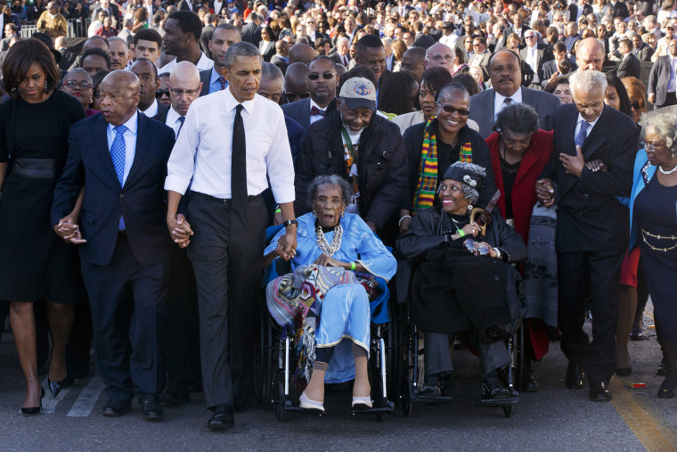 Amelia Boynton Robinson, center, who was beaten during \"Bloody Sunday,\" holds President Barack Obama's hand as they walk across the Edmund Pettus Bridge in Selma, Ala., Saturday, March 7, 2015. (Photo by Jacquelyn Martin/AP)