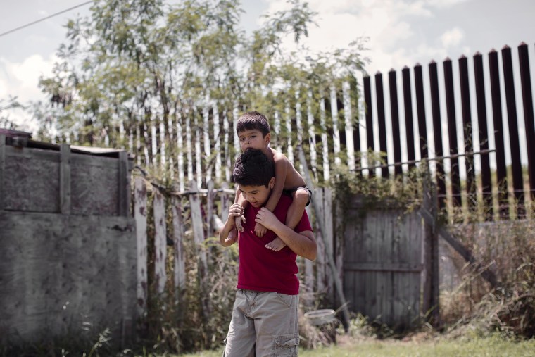 Damian Juarez, a boy whose backyard is lined by the border fence, plays with his little brother in Brownsville, Texas. (Photo by Bryan Schutmaat for MSNBC)