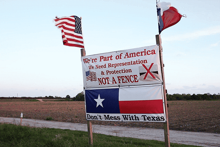 American and Texan flags flap in strong winds atop a sign built by Pamela Taylor protesting the border fence in Brownsville, Texas. (Photo by Bryan Schutmaat for MSNBC)