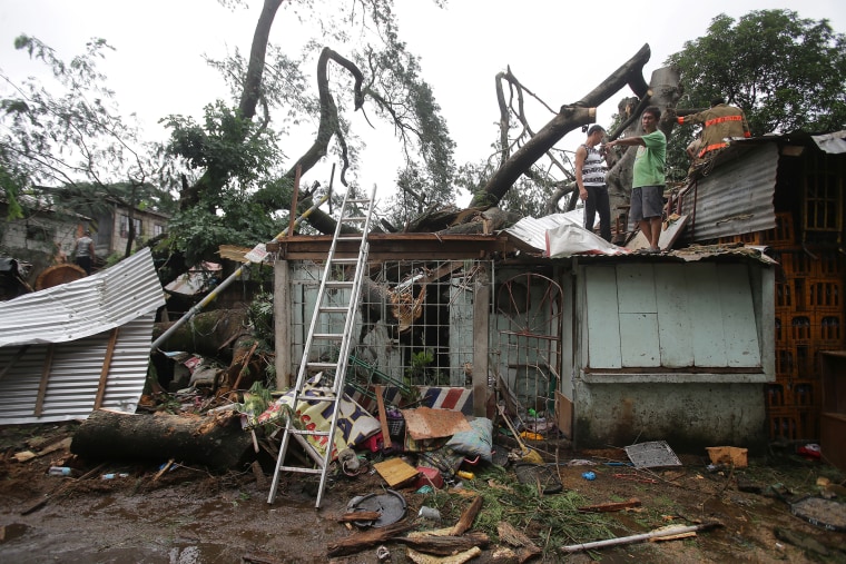 Residents and rescuers stand on top of a damaged house as they cut apart a toppled tree from Typhoon Koppu in suburban Quezon city, north of Manila, Philippines on Oct. 19, 2015.