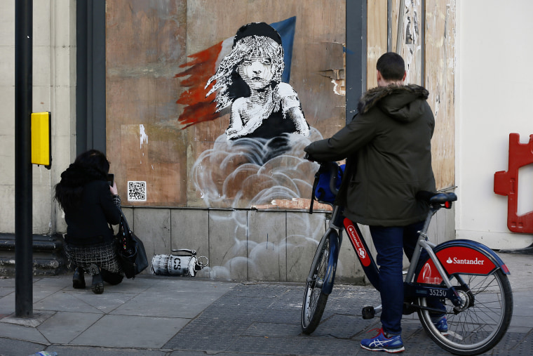 People photograph a new graffiti mural attributed to Banksy, opposite the French embassy in London, Jan. 25, 2016. (Photo by Stefan Wermuth/Reuters)