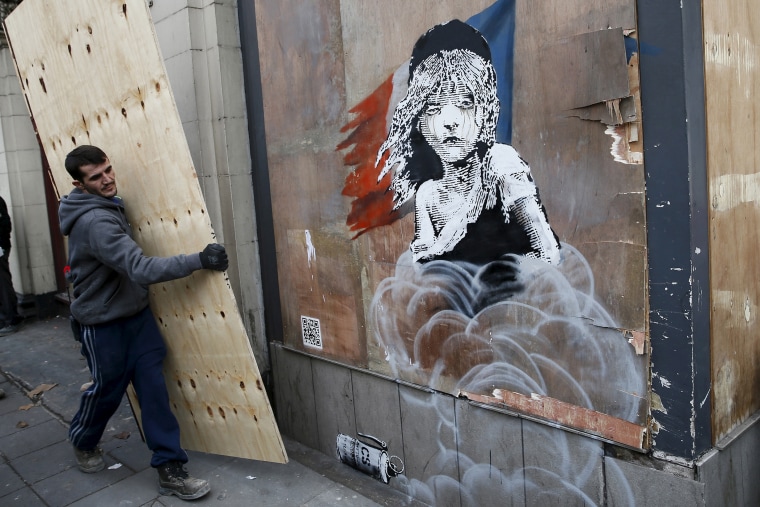 A worker carries a board to cover a new graffiti mural attributed to Banksy, opposite the French embassy in London, Jan. 25, 2016. (Photo by Stefan Wermuth/Reuters)