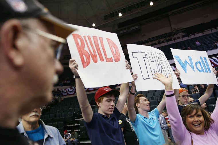 People hold signs that read, \" Build that Wall\", as they wait for the start of a campaign rally for Republican presidential candidate Donald Trump at the University of South Florida on Feb. 12, 2016 in Tampa, Fla. (Photo by Joe Raedle/Getty)