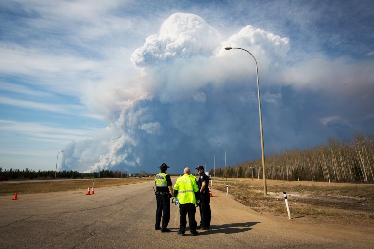 Officers look on as smoke from Fort McMurray's raging wildfires billow into the air after their city was evacuated, May 4, 2016. (Photo by Topher Seguin/Reuters)