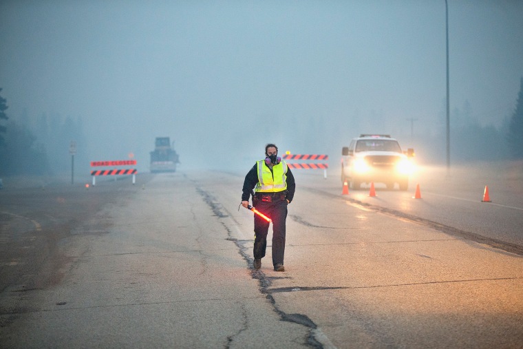 Smoke fills the air as a police officer stands guard at a roadblock along Highway 63 leading into Fort McMurray on May 8, 2016 near Fort McMurray, Alberta, Canada. (Photo by Scott Olson/Getty)