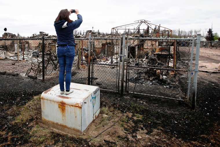 A woman takes photos of the burned remains of a house in the Abasand neighbourhood of Fort McMurray, Alberta, Canada, May 9, 2016 after wildfires forced the evacuation of the town. (Photo by Chris Wattie/Reuters)