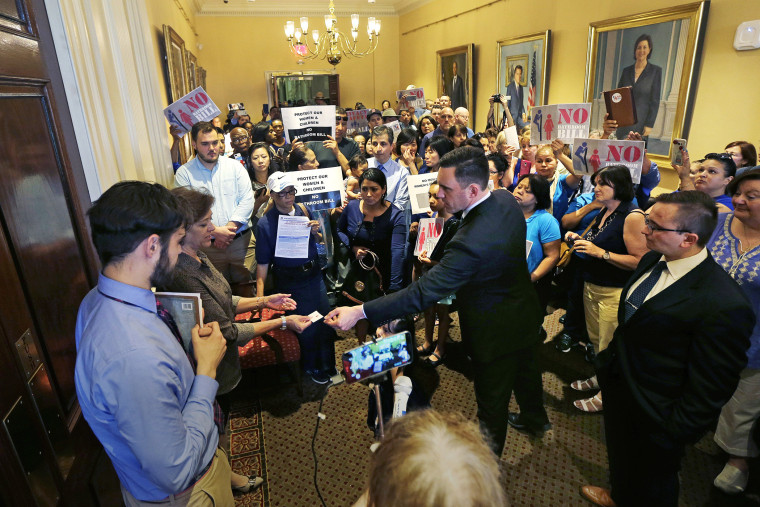 Andrew Beckwith, president of Massachusetts Family Institute, hands his business card to members of Governor Baker's staff, who block the door to his office, as protestors gather at the Statehouse in Boston, June 1, 2016. (Photo by Charles Krupa/AP)