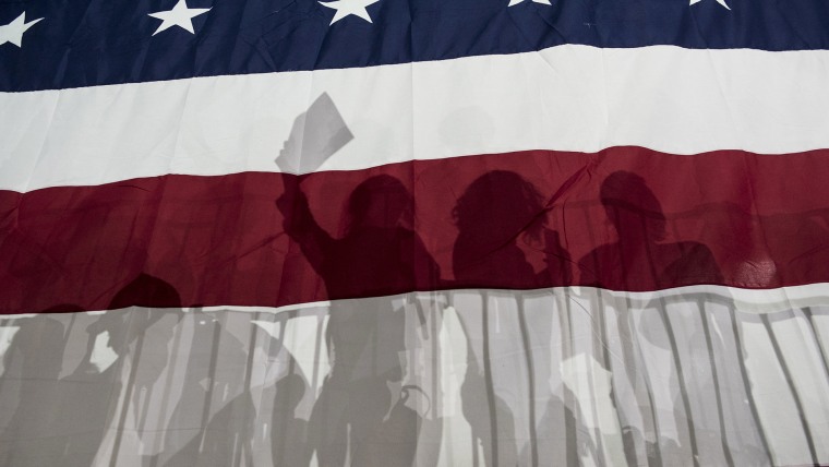 Political supporters are silhouetted in a large American flag on March 2, 2016. (Photo by Andrew Renneisen/Getty)