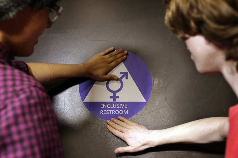 Two students place a new sticker on the door at the ceremonial opening of a gender neutral bathroom at Nathan Hale High School on May 17, 2016 in Seattle, Wash. (Photo by Elaine Thompson/AP)