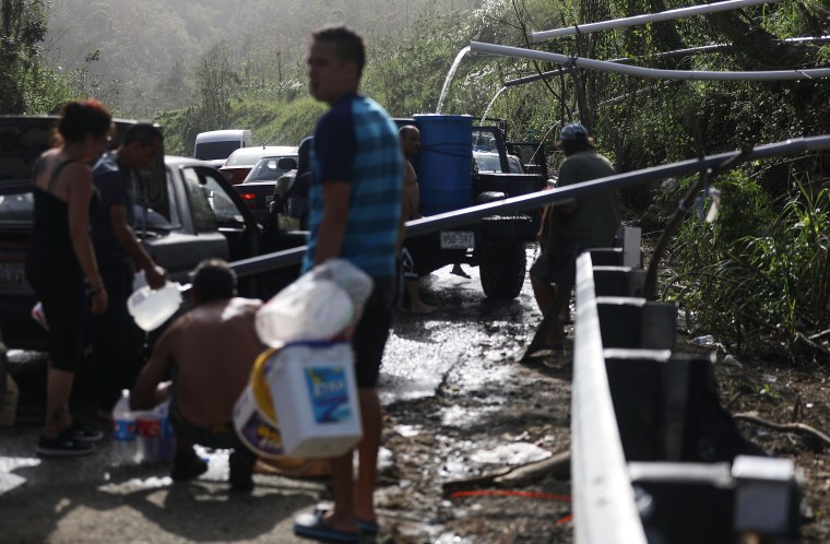 People fill containers with water funneled with pipes from a mountain stream in Utuado, Puerto Rico.